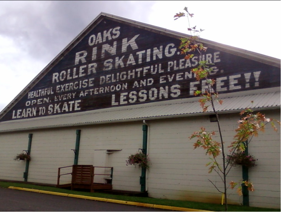 A brown and white a frame barn with white painted lettering that reads "Oaks Rink Roller Skating"