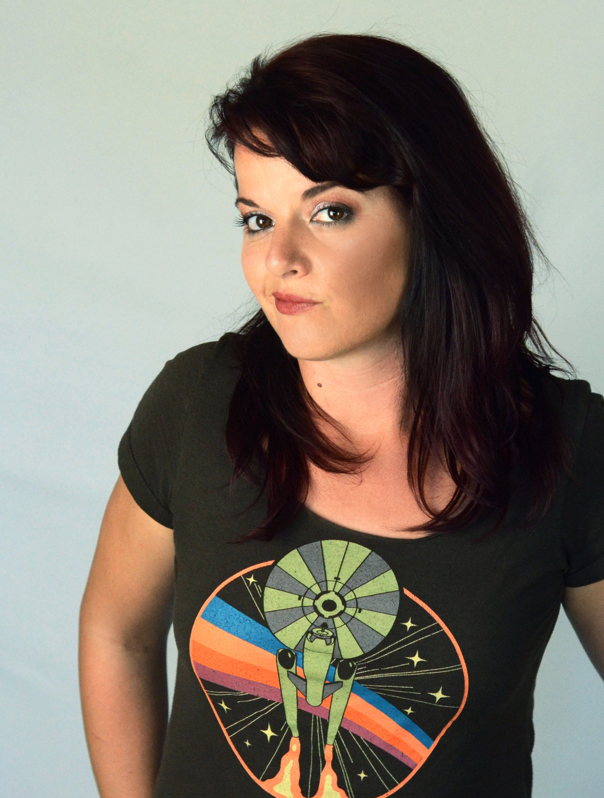 An auburn haired woman wearing a brown vintage tee with a space ship that looks like The Enterprise from Star Trek.